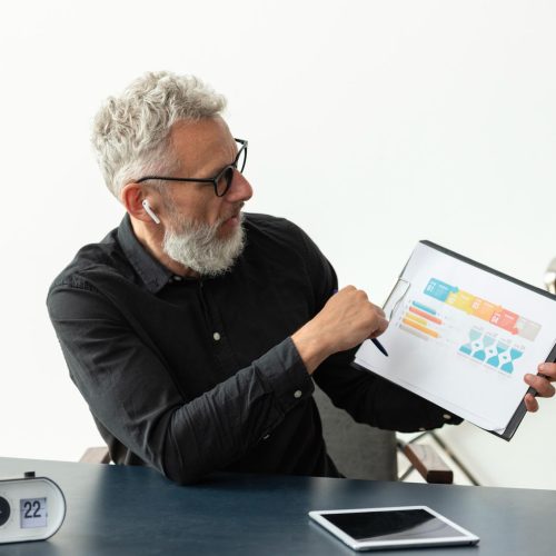 older-man-home-showing-graph-notepad-with-tablet-desk-2